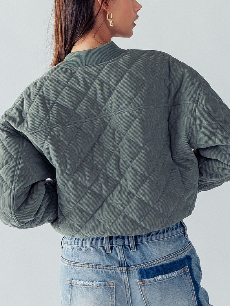 Puede incluir: Una chaqueta acolchada de pana verde con cuello alto y mangas largas. La chaqueta es corta y tiene un patr&oacute;n de acolchado en forma de diamante.