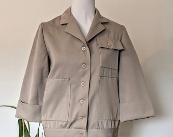 May include: A beige button-up jacket with a collared neckline and two large pockets on the front. The jacket has long sleeves with buttoned cuffs.