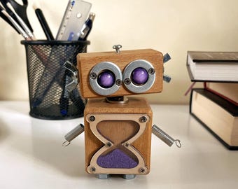 May include: A wooden robot figurine with a square body and head, featuring purple eyes and a purple hourglass design on the front. The robot has metal accents and spring arms, sitting on a white surface.