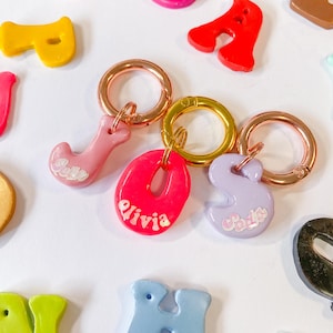 May include: A set of colourful, personalised keychains with the names "Bella", "Olivia", and "Sophie" written on them. The keychains are attached to gold and rose gold split rings.