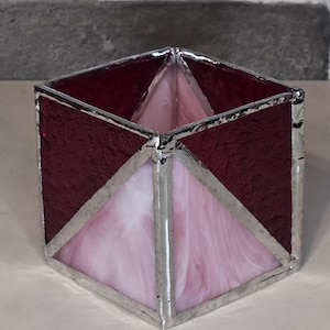 May include: A square glass candle holder with a pink and burgundy stained glass design. The holder has a silver trim around the edges.