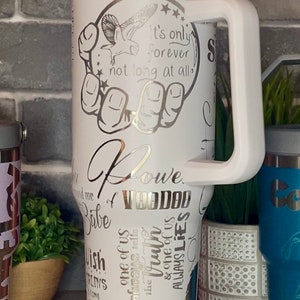 May include: White stainless steel tumbler with a silver design featuring an owl, stars, and the text "It's only forever not long at all". The tumbler also has the text "Lowe" and "Babe of VOODOO" with other words and phrases in a silver design.