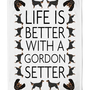 Może przedstawiać: Biały ręcznik kuchenny z czarnym tekstem, który brzmi "Life is better with a Gordon Setter". Tekst jest otoczony obramowaniem czarno-brązowych ilustracji psa rasy Gordon Setter.
