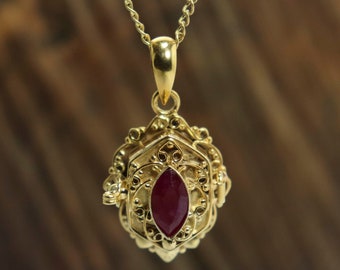 May include: A gold pendant necklace with a detailed filigree design and a red gemstone in the center.