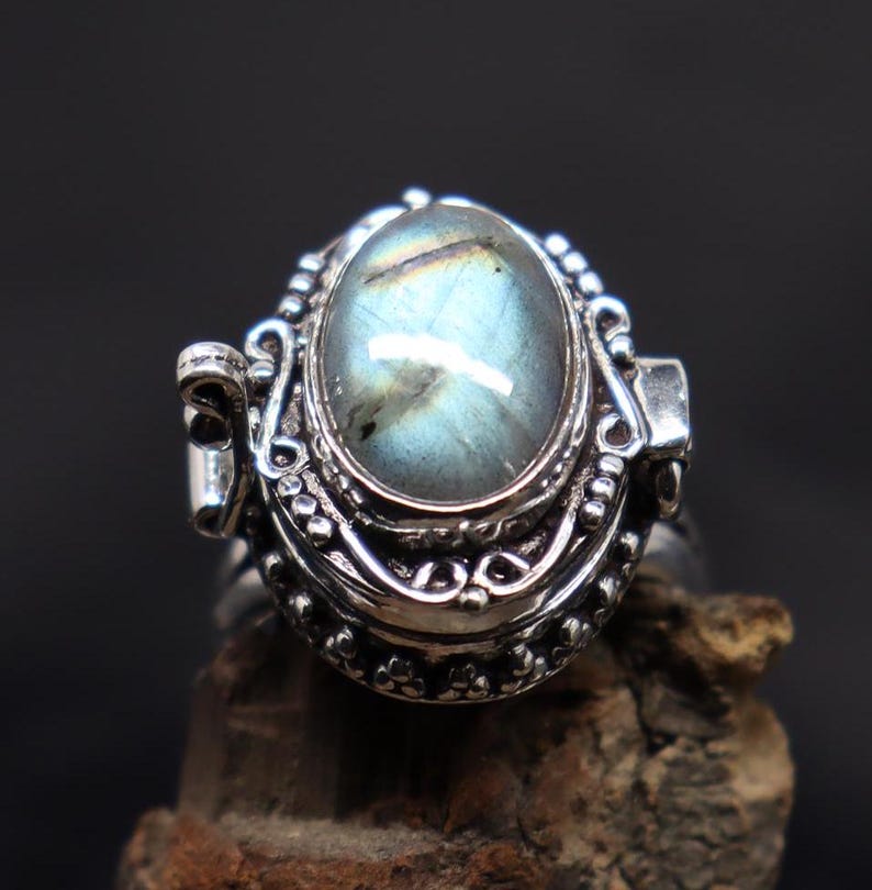 Op de afbeelding: Een zilveren ring met een scharnierend medaillon met een blauwe en groene labradorit edelsteen. Het medaillon heeft ingewikkelde zilveren details en een parelrand.