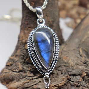 May include: A silver pendant featuring a blue labradorite gemstone set in a silver bezel. The pendant has a silver chain and a silver bail.