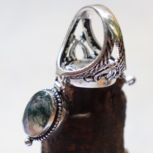 Puede incluir: Un anillo de plata con un colgante de &aacute;gata verde. El anillo tiene un dise&ntilde;o intrincado y la piedra es de color verde claro con vetas verde oscuro.