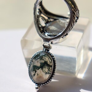 Puede incluir: Un anillo de plata con un dise&ntilde;o intrincado y un colgante ovalado colgante con una piedra de &aacute;gata musgosa con patrones verdes y blancos.