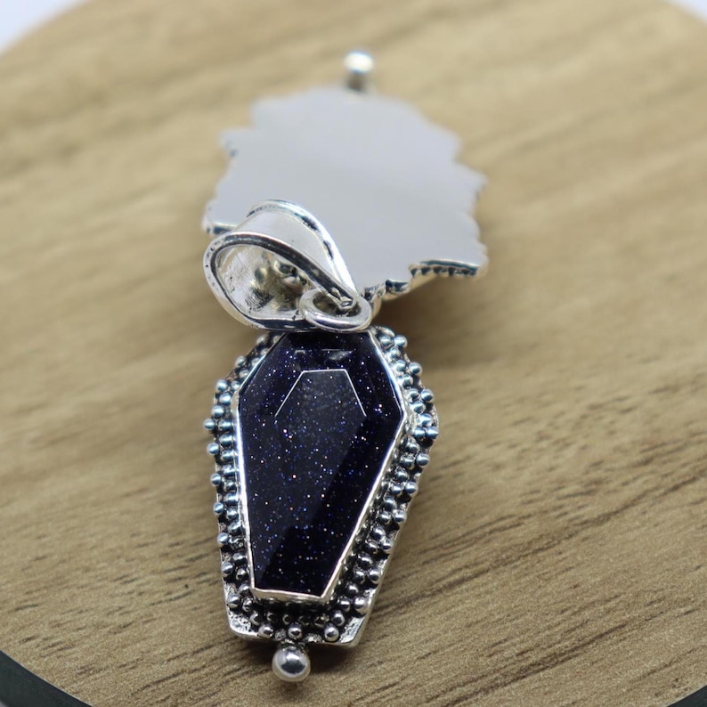 Puede incluir: Pendiente de plata con una piedra negra en forma de ata&uacute;d y una anilla de plata. La piedra est&aacute; engastada en un marco de plata con un dise&ntilde;o detallado.