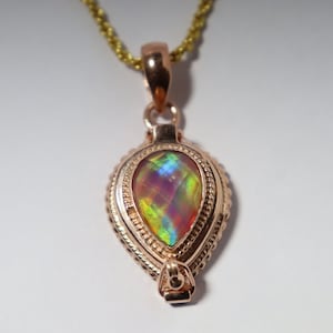 May include: A teardrop-shaped pendant with a multi-colored iridescent gemstone set in a gold-toned metal frame.