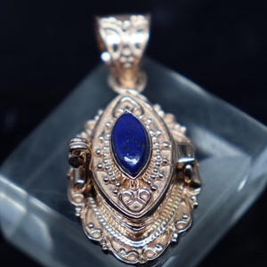 Puede incluir: Un colgante de plata con un medallón adornado y una piedra de lapislázuli azul.