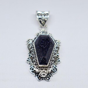 Puede incluir: Colgante de plata con una piedra preciosa negra en forma de ata&uacute;d. El colgante tiene un dise&ntilde;o ornamentado con detalles intrincados.