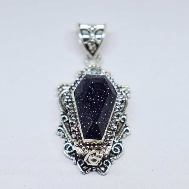 Puede incluir: Colgante de plata con una piedra preciosa negra en forma de ata&uacute;d. El colgante tiene un dise&ntilde;o ornamentado con detalles intrincados.