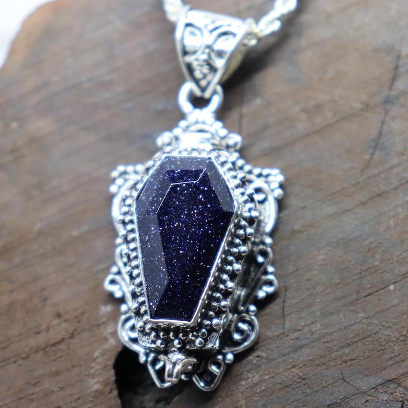 Puede incluir: Un collar con un colgante de plata adornado con una piedra azul oscuro brillante en forma de ata&uacute;d. El colgante est&aacute; decorado con filigranas de plata.