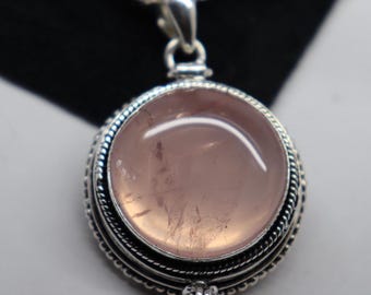 Puede incluir: Un colgante de plata con un medallón redondo de cuarzo rosa claro. El medallón tiene un diseño de plata detallado y una abertura con bisagra.