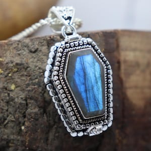 May include: A silver pendant in the shape of a coffin with a blue labradorite gemstone inside.