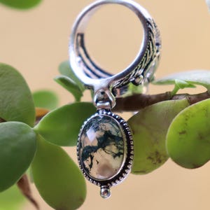 Puede incluir: Un anillo de plata con una piedra de &aacute;gata musgosa ovalada colgante. El anillo tiene una banda texturizada y la piedra est&aacute; engastada en un engaste de plata.