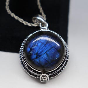 May include: A silver pendant necklace with a round blue labradorite gemstone. The pendant has a detailed silver border and a silver bail.