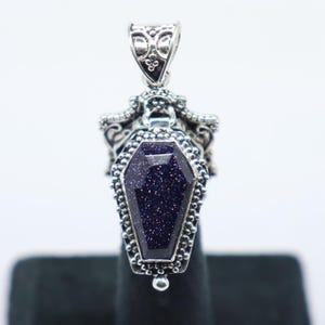 Puede incluir: Colgante de plata con un dise&ntilde;o detallado en forma de ata&uacute;d con una piedra azul oscuro brillante.