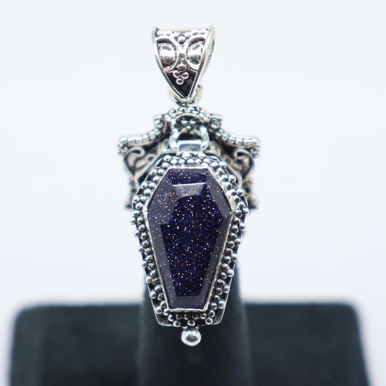 Puede incluir: Colgante de plata con un dise&ntilde;o detallado en forma de ata&uacute;d con una piedra azul oscuro brillante.