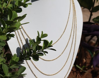 May include: A gold chain necklace with four strands of varying lengths. The necklace is displayed on a white mannequin bust.