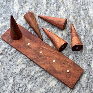 May include: A rectangular wooden base with four small circular metal inserts and four separate wooden cones. The cones have flat circular bases with small metal discs, allowing them to be placed upright on the wooden board's metal inserts.