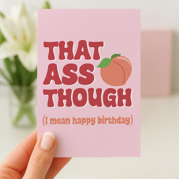 May include: A rectangular greeting card with a light pink background. The text reads "THAT ASS THOUGH" in bold red letters, accompanied by a peach illustration. Below, the text "(I mean happy birthday)" is printed in a smaller, lighter red font.