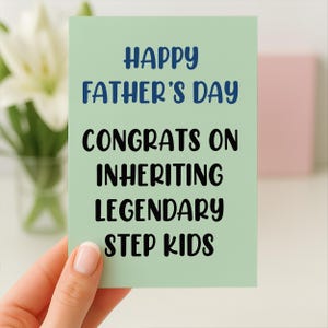 Op de afbeelding: Een lichtgroene Vaderdagkaart met de tekst "HAPPY FATHER'S DAY" in blauw en "CONGRATS ON INHERITING LEGENDARY STEP KIDS" in zwart. De kaart wordt door een hand vastgehouden.