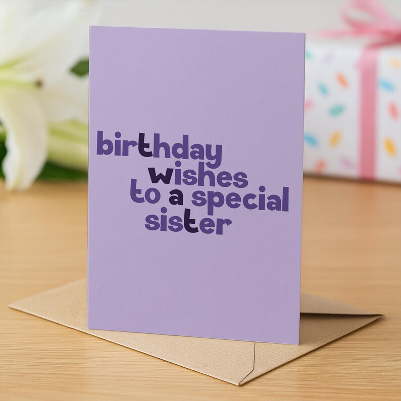 May include: A lavender birthday card with the text "birthday wishes to a special sister" in a dark purple font. The card is on a brown envelope, with a blurred background of a white flower and a wrapped gift.