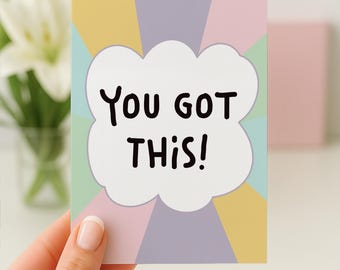 Puede incluir: Una tarjeta de felicitación rectangular con un bocadillo de diálogo blanco en forma de nube en el centro, con el texto negro "YOU GOT THIS!" impreso en una fuente negrita y redondeada. El fondo presenta franjas radiales en colores pastel amarillo, lavanda, rosa y verde menta.