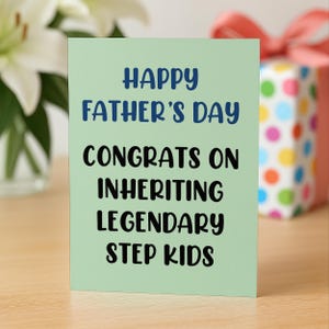 Op de afbeelding: Een lichtgroene Vaderdagkaart met de tekst "HAPPY FATHER'S DAY CONGRATS ON INHERITING LEGENDARY STEP KIDS" in blauwe en zwarte tekst. Een cadeauverpakking met een rode strik staat op de achtergrond.