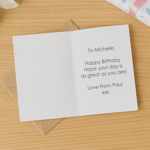 May include: A white folded greeting card with black printed text that reads: To Michelle, Happy Birthday Hope your day is as great as you are! Love From Paul XXX. The card is positioned on top of a brown kraft paper envelope.