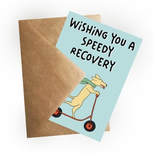 Op de afbeelding: Een lichtblauwe kaart met de tekst "Wishing you a speedy recovery" in het zwart. Een gele cartoonhond met een groene sjaal rijdt op een rode scooter op de kaart.