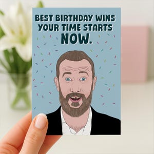 Może przedstawiać: Kartka urodzinowa z kreskówkową ilustracją mężczyzny z brodą i niebieskimi oczami. Karta zawiera napis "BEST BIRTHDAY WINS YOUR TIME STARTS NOW." na jasnoniebieskim tle z konfetti.
