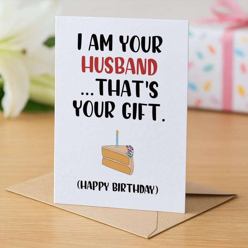 May include: A white greeting card with black and red text that reads I AM YOUR HUSBAND ... THAT'S YOUR GIFT. (HAPPY BIRTHDAY). Below the text is a simple illustration of a single slice of cake with a blue candle and colorful sprinkles on top.