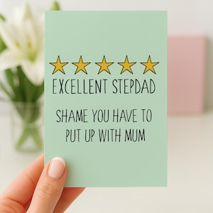 May include: A light green greeting card with the text "EXCELLENT STEPDAD SHAME YOU HAVE TO PUT UP WITH MUM" and five gold stars. The card is held by a person.