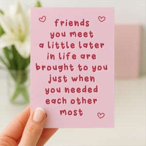May include: A pink greeting card with the text "friends you meet a little later in life are brought to you just when you needed each other most" in red. The card has three small heart illustrations.
