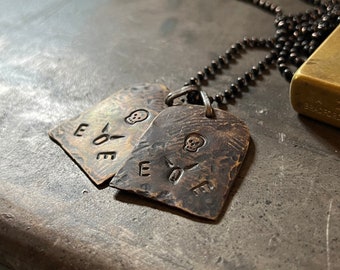 May include: Two silver-toned dog tags with a skull and crossbones design and the word "EVE" engraved on each tag. The tags are attached to a black chain necklace.