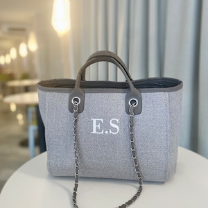 May include: A grey tote bag with a chain strap and the initials "E.S." embroidered on the front.