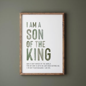 Op de afbeelding: Een ingelijste print met de tekst "I AM A SON OF THE KING" in groene letters. De print bevat ook extra tekst onder de hoofdzin. De lijst is van hout en wordt weergegeven tegen een donkergroene muur.