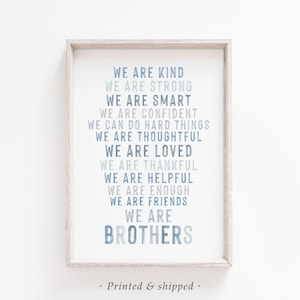 May include: Framed print with a white background and light blue text. The text reads "WE ARE KIND, WE ARE STRONG, WE ARE SMART, WE ARE CONFIDENT, WE CAN DO HARD THINGS, WE ARE THOUGHTFUL, WE ARE LOVED, WE ARE THANKFUL, WE ARE HELPFUL, WE ARE ENOUGH, WE ARE FRIENDS, WE ARE BROTHERS."