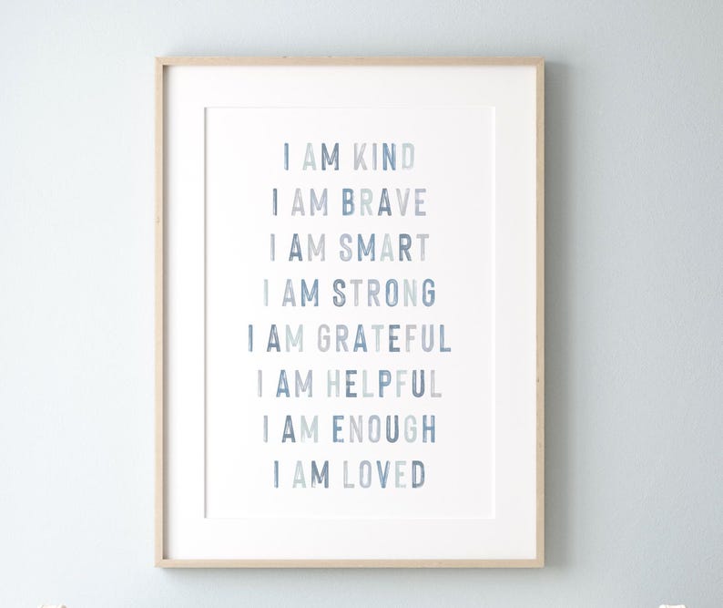 以下が含まれることがあります： 「I AM KIND, BRAVE, SMART, STRONG, GRATEFUL, HELPFUL, ENOUGH, LOVED」という言葉が様々な青色で書かれたフレーム入りのプリント。テキストは白い背景に配置され、明るい木製のフレームに収められています。