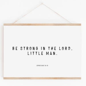 Könnte beinhalten: Gerahmter Druck mit dem Text "BE STRONG IN THE LORD, LITTLE MAN." in Schwarz, darunter "EPHESIANS 6:10". Der Druck ist weiß mit einem Naturholzrahmen und wird an einer Schnur aufgehängt.