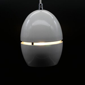 May include: A modern, white pendant light fixture with a spherical design. The light is divided into two sections, with a thin illuminated gap in the middle. A white cord suspends the light against a black background.
