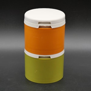 Può includere: Un set di contenitori cilindrici impilabili composto da due sezioni distinte. La sezione superiore è di un arancione vivace, mentre quella inferiore è di un verde oliva tenue. Ogni sezione è completata da un coperchio di colore bianco.