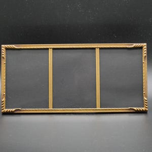May include: A rectangular triple picture frame with a metallic gold finish. The frame features a textured, rope-like border pattern with decorative corner accents and two vertical dividers, creating three distinct sections with black inserts.