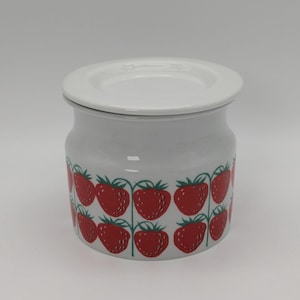 Könnte beinhalten: Weiße Keramikdose mit Deckel, verziert mit einem sich wiederholenden Muster aus roten Erdbeeren mit grünen Stielen und Blättern.