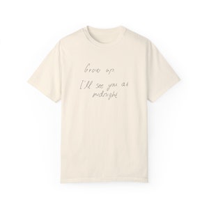 Puede incluir: Una camiseta beige con el texto "Grow up? I'll see you at midnight" escrito en tinta negra.