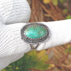 May include: Oval turquoise ring with a silver setting. The turquoise stone is a vibrant teal colour, set within a detailed silver frame. The ring's band splits into two at the base of the setting.