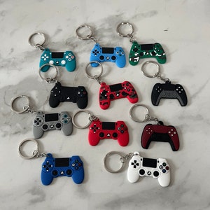 May include: A set of 10 colourful keychains shaped like a Playstation controller. The keychains are made of silicone and come in a variety of colours, including blue, green, red, black, and white.